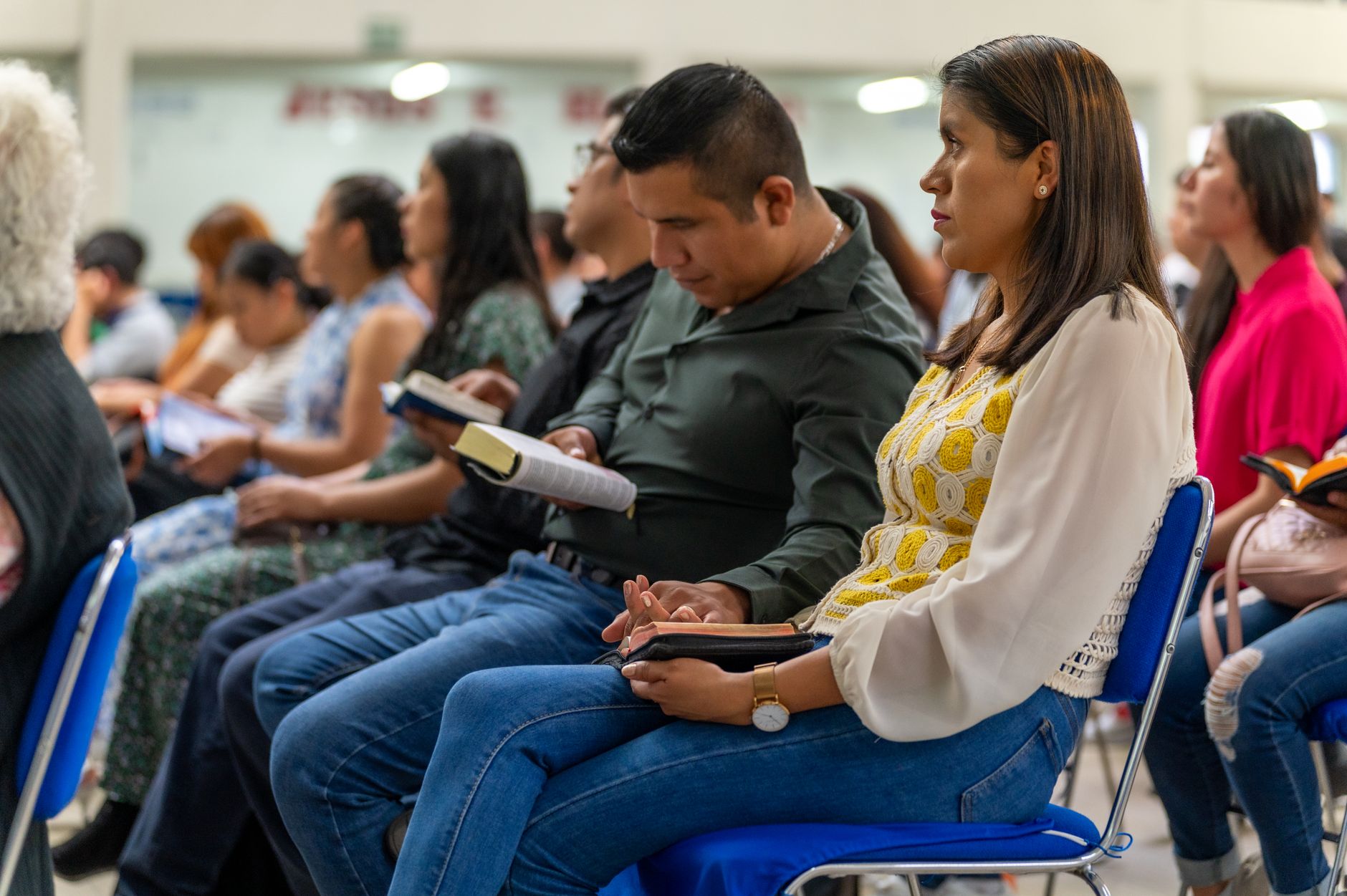 Men and women attending a Christian meeting in Ciudad de México, reading books indoors.