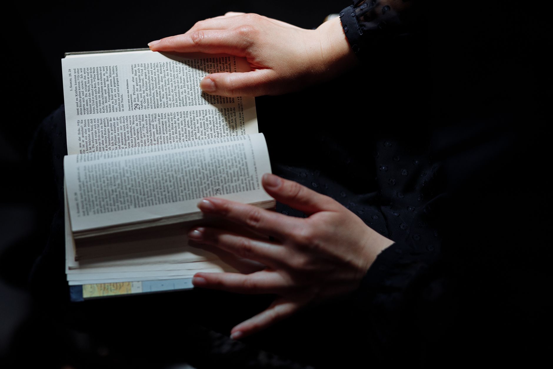 Close-up of hands holding an open book in dim lighting, emphasizing a serene, reflective moment.