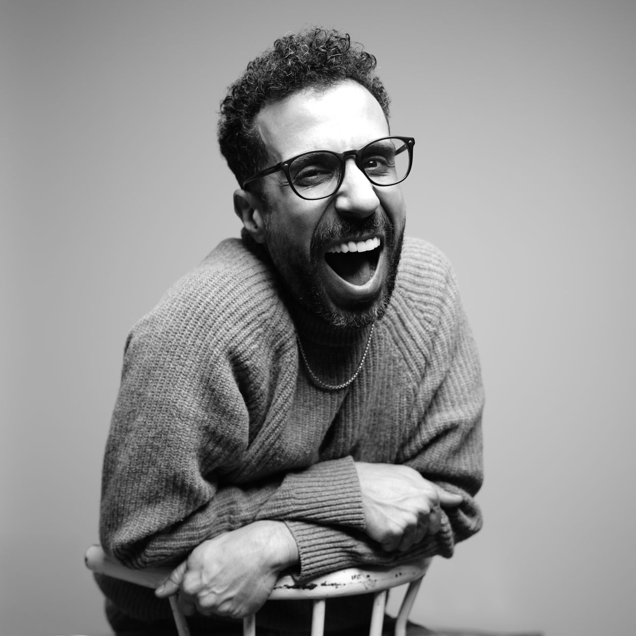 A candid black and white studio portrait of a man with glasses laughing joyfully.