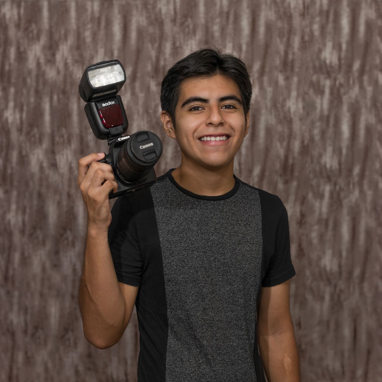 A joyful portrait of a young man smiling broadly, wearing a stylish black hat.